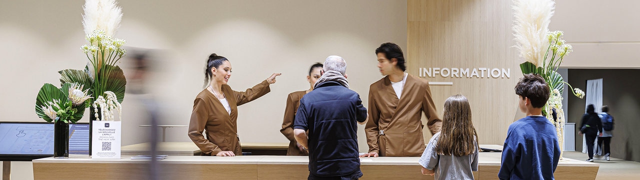 Reception desk with staff in brown uniforms assisting visitors.